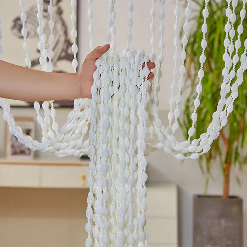 A hand is pulling a white decorative fabric door curtain with tassel trim, featuring numerous white pom-poms.