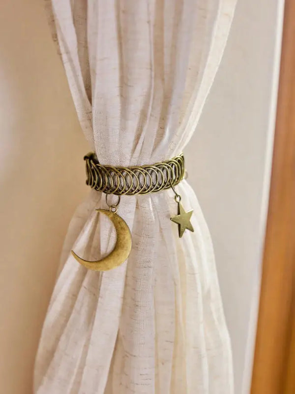 A vintage metal curtain clip featuring a woven band, a crescent moon charm, and a star charm against a light fabric.
