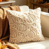 A cream-colored fuzzy throw pillow with a textured maple leaf pattern resting on a light sofa next to a tan blanket.