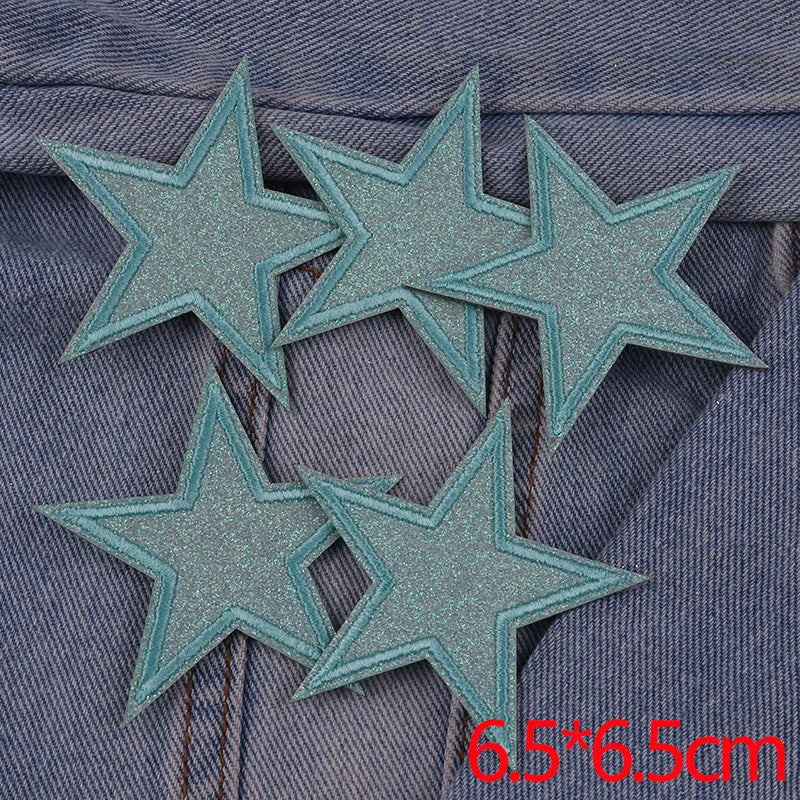 Five glitter iron-on embroidered star patches on a denim fabric background.