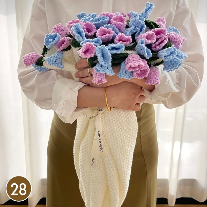 A person holds a hand knitted floral rose bouquet and a cream colored throw blanket.