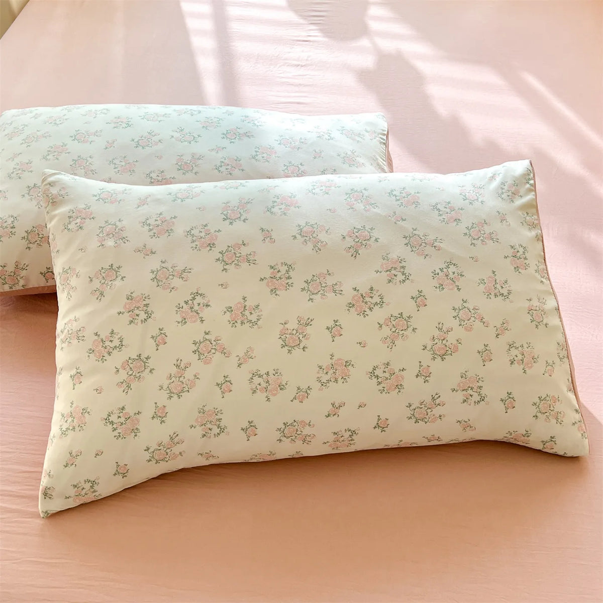 A light green floral printed pillow cover resting on a pink surface with shadows.