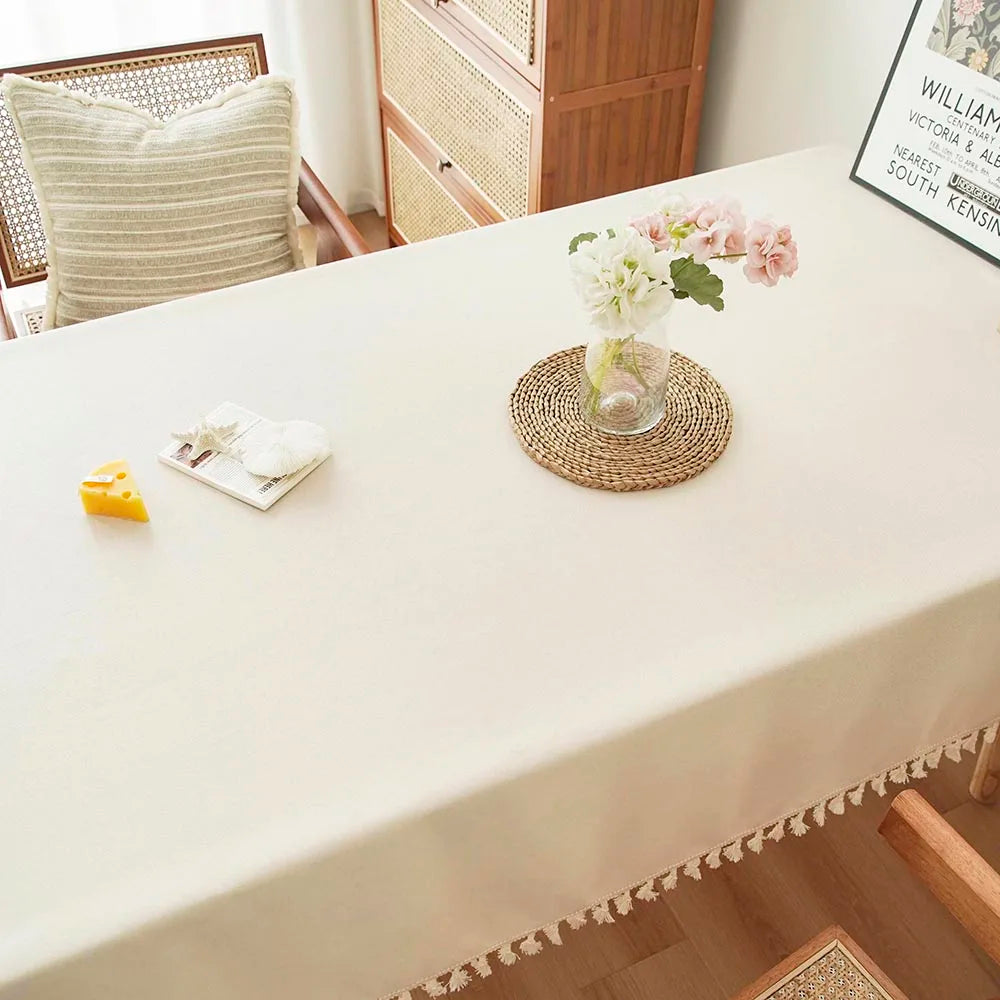 A close-up of a white tablecloth with textured cotton tassel table runners and floral arrangements.