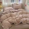 A beige floral bedding set with ruffled edges is displayed on a bed next to a window.