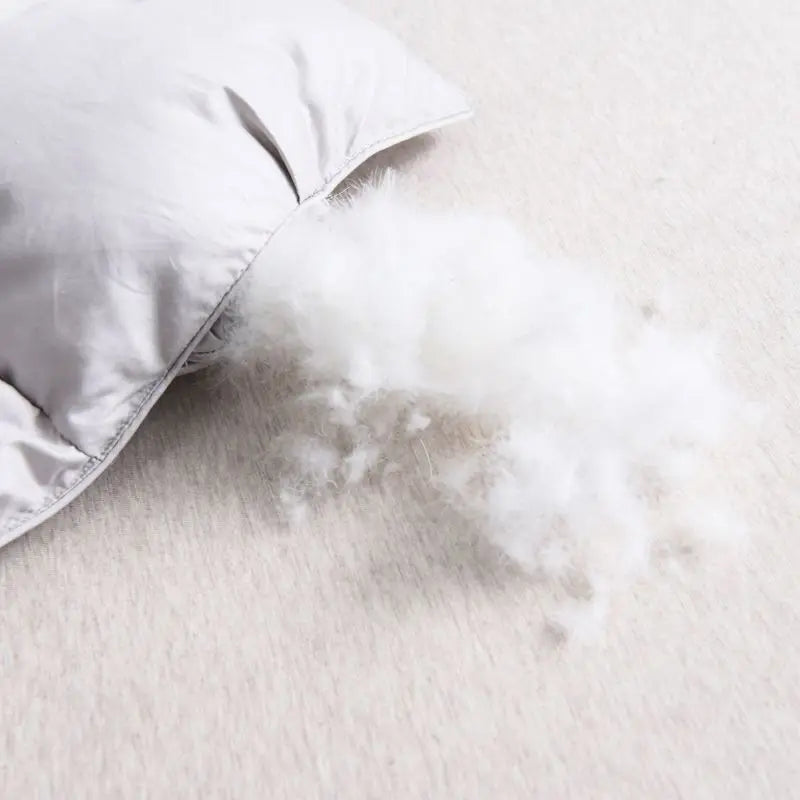 A close-up of a white luxury goose down duvet blanket with fluffy white down spilling out onto a light surface.