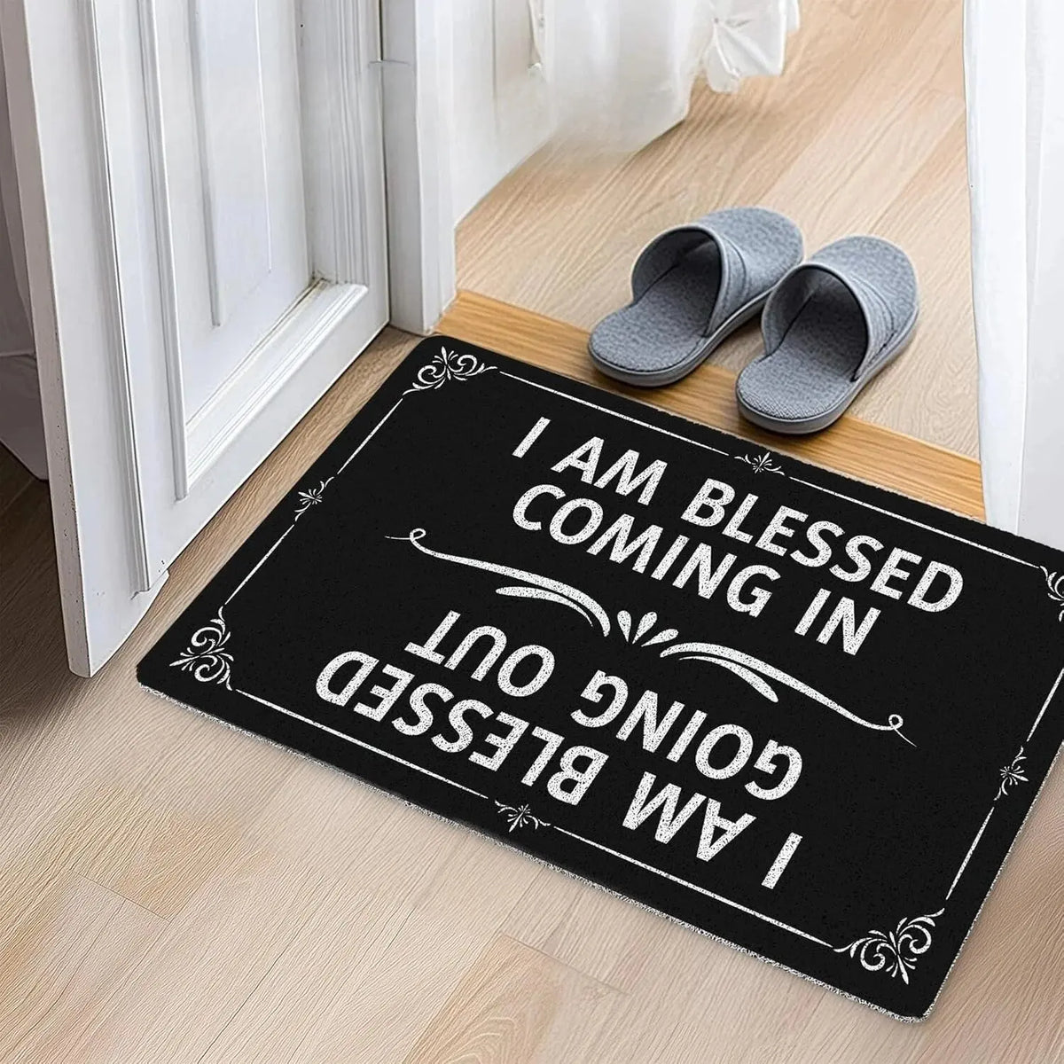 Black doormat with white text saying I am blessed coming in I am blessed going out placed on a wooden floor near a white door