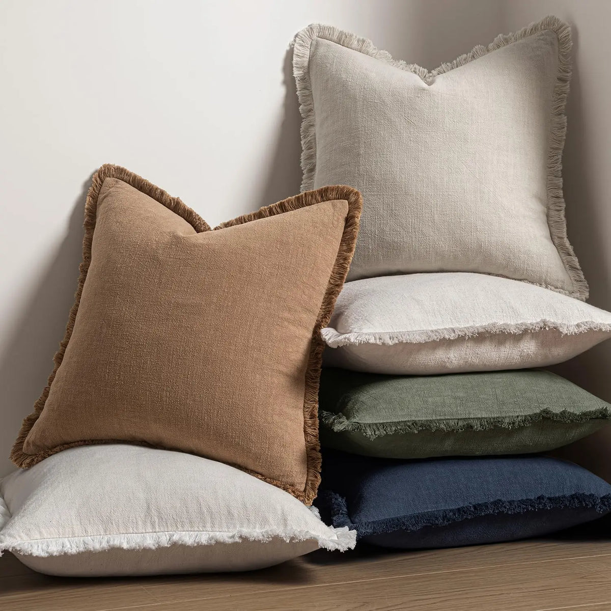 A stack of linen fringe throw pillow covers in beige, cream, and deep blue colors.