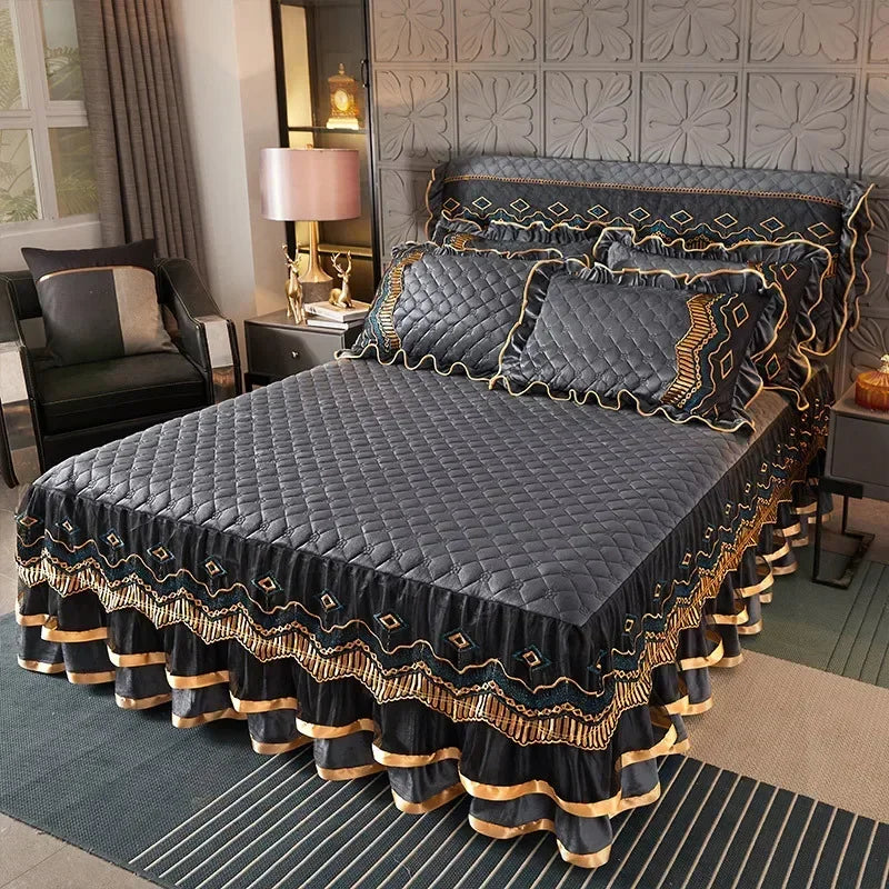 A dark gray quilted bed skirt with gold trim is displayed on a bed, set against a textured wall.