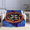 A purple and blue printed flannel travel blanket featuring a black and white rock design on an orange circle.