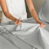 A person's hands are smoothing a gray microfiber bed sheet set on a bed.