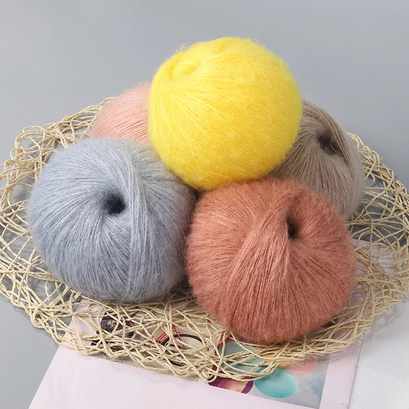 A pile of yellow, gray, and pink mohair yarn balls displayed on a woven net.