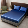 A modern bedroom featuring a bed with blue and navy satin bedding, dark brown headboard, and a green upholstered chair.