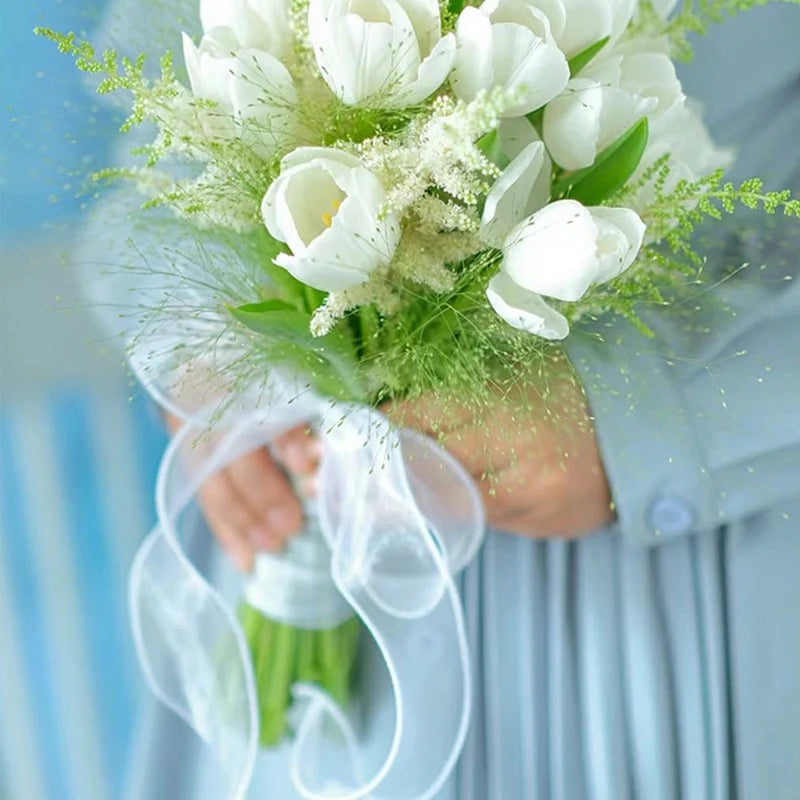 A bouquet of white tulips and greenery tied with a sheer white organza ribbon for gift wrapping or crafts.