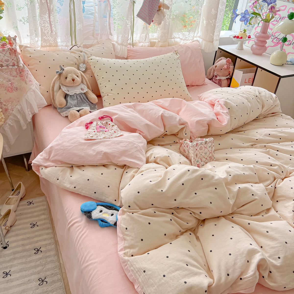 A pink polka dot duvet cover set with matching pillowcases and stuffed animal toys on a bed.