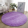 A fluffy purple shaggy round area rug placed on a light wood floor next to a sofa and a potted plant.