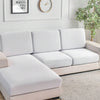 A modern, light beige sofa with white slipcovers sits in a bright room next to a framed motivational poster and a clock.