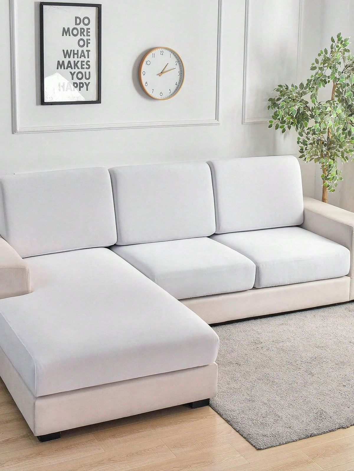 A modern, light beige sofa with white slipcovers sits in a bright room next to a framed motivational poster and a clock.