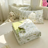 A stack of white and green quilted blankets and pillows with leafy patterns displayed on a light-colored surface.