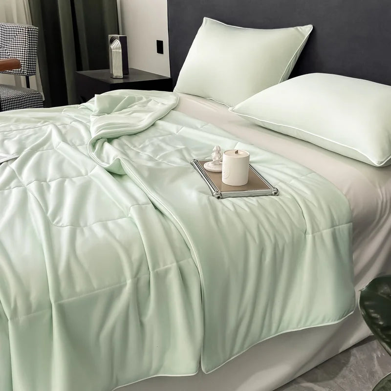 A light mint green reversible cooling quilt is displayed on a bed with white pillows and a dark gray wall.