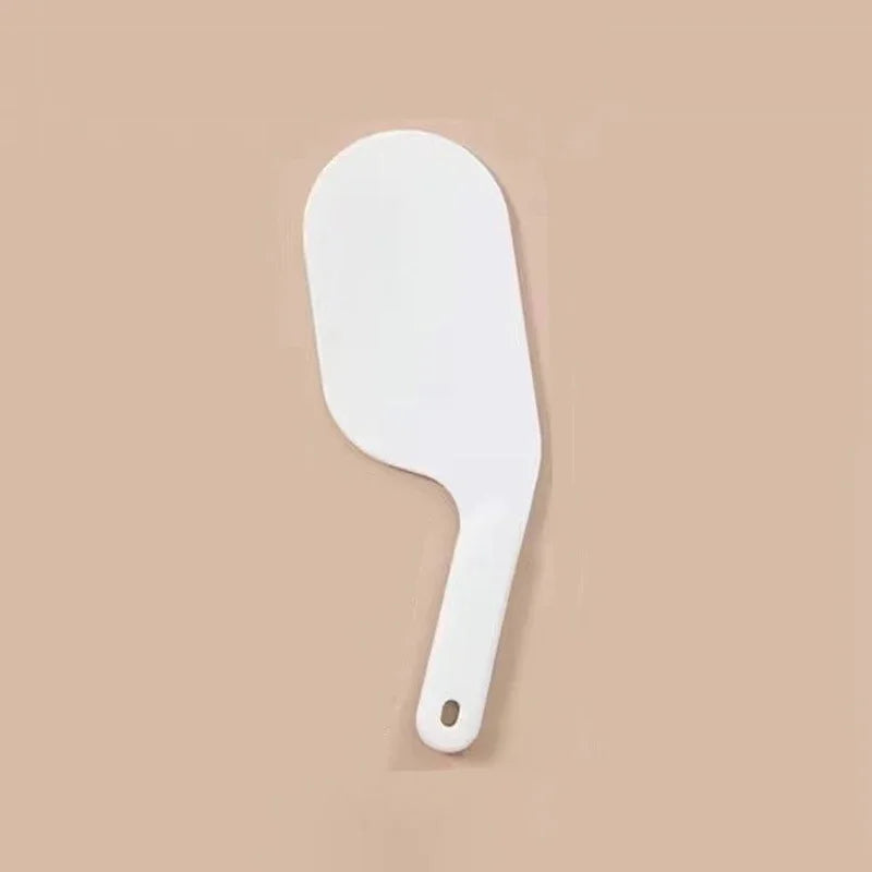 A white bed sheet folding and organizing tool with a curved handle is shown against a beige background.