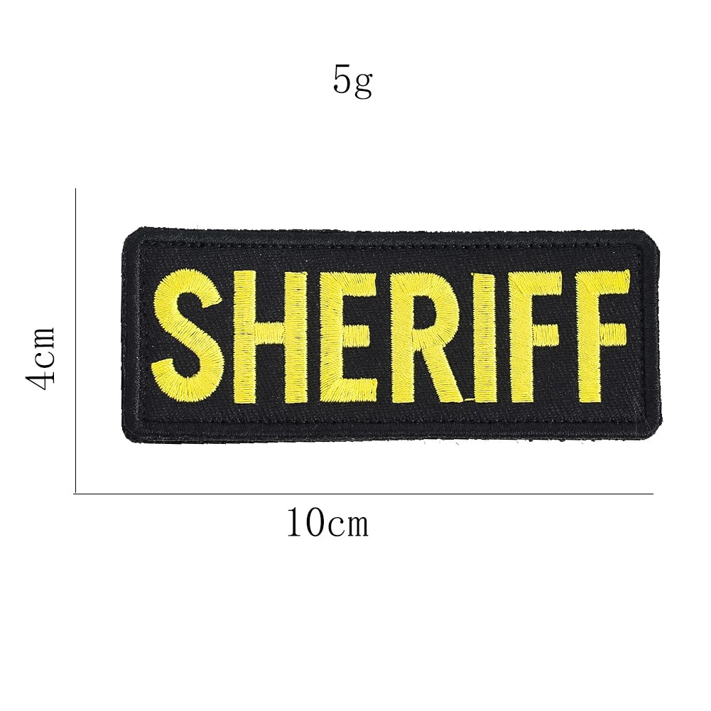 Black embroidered patch with yellow text spelling out SHERIFF on a fabric background.