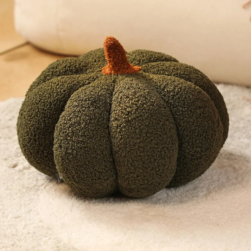 A plush, olive green pumpkin throw pillow with a textured surface rests on a light fabric.