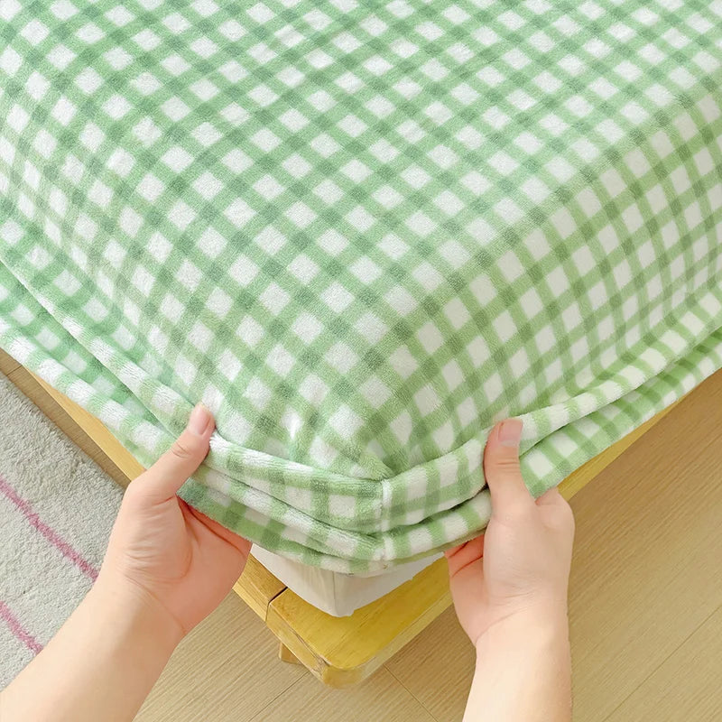 Hands are pulling up a green and white checkered flannel fitted sheet with deep pockets.