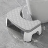 A gray adjustable adult toilet squat stool with a diamond-patterned seat is shown on a tile floor.