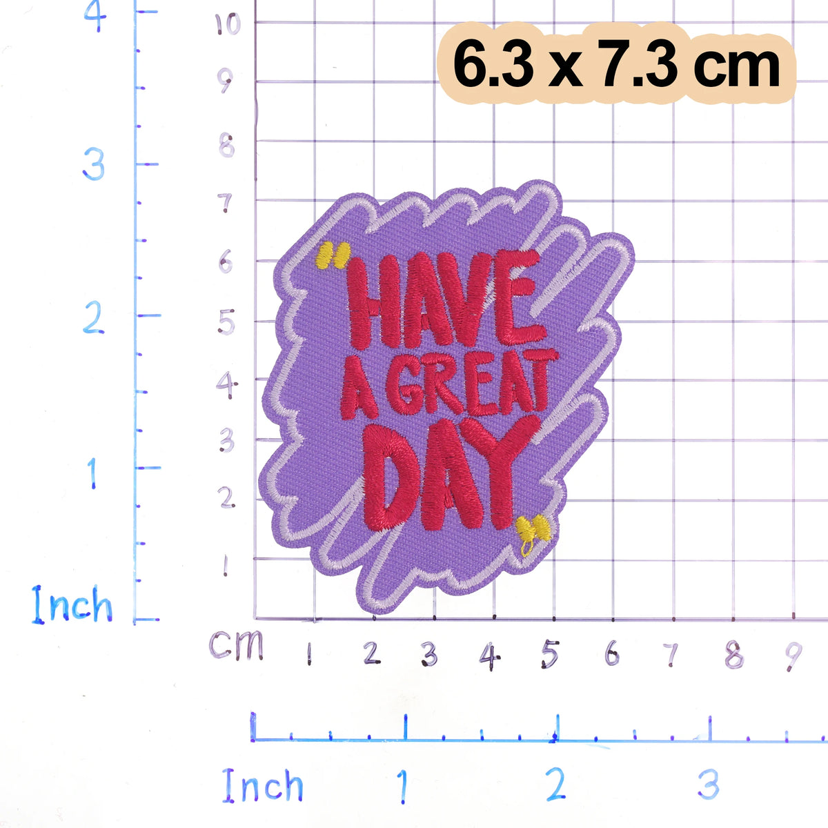 A purple iron-on embroidered patch with the text HAVE A GREAT DAY on a white grid background.