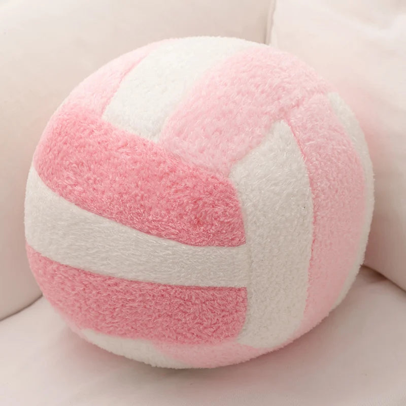 A pink and white striped plush volleyball ball cushion resting on a light surface.
