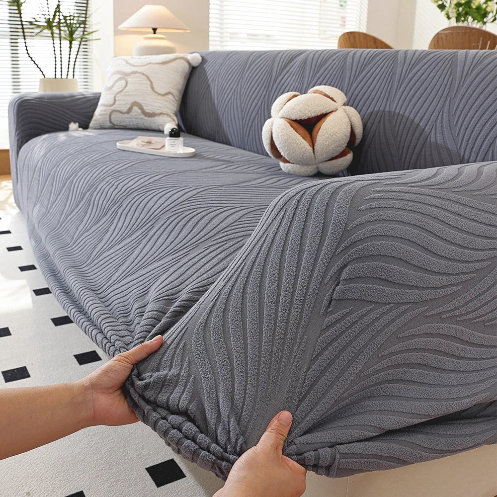 A hand is adjusting a gray, ribbed stretch sofa cover featuring an elegant plant pattern and an elastic edge.