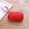 A ball of bright red flat thread yarn lying on a wooden surface next to a white wire mesh basket and a framed flower arrangem