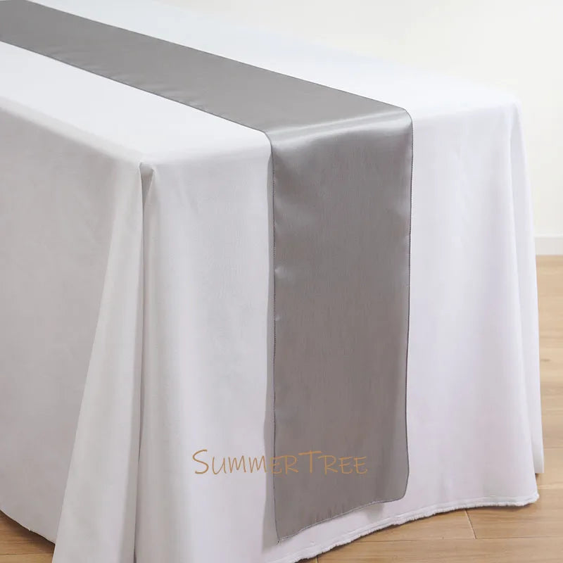 Elegant satin table runner in silver gray draped across a white tablecloth.