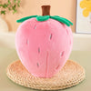 A pink plush strawberry throw pillow resting on a woven straw mat.