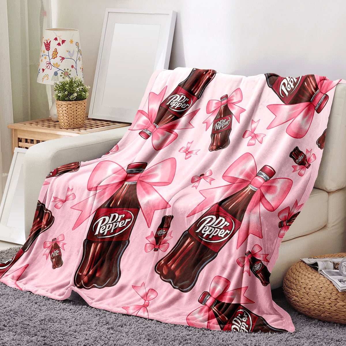 A pink cozy blanket featuring a repeating pattern of Dr. Pepper bottles tied with pink ribbons.