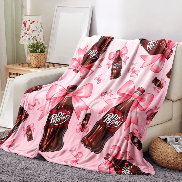 A pink cozy blanket featuring a repeating pattern of Dr. Pepper bottles tied with pink ribbons.