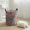 A foldable leopard print laundry basket with black handles sits on a woven mat next to a white window.
