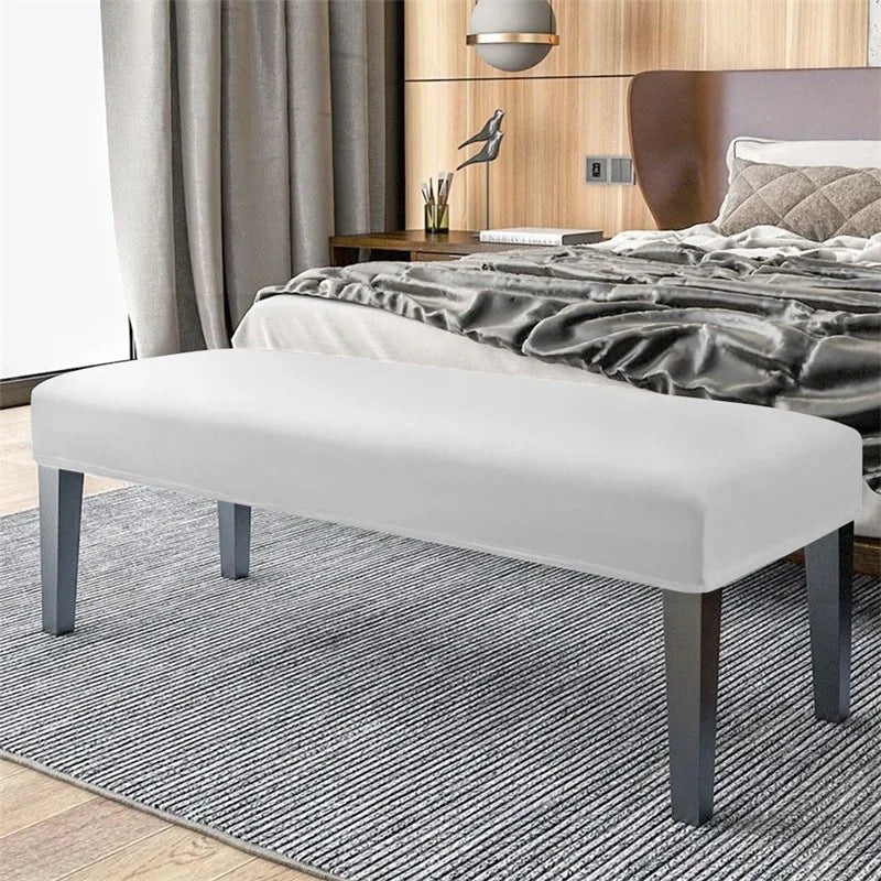 A modern white bench with dark legs and a slipcover is placed on a gray striped rug in a bedroom setting.