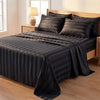 A dark gray striped satin bedding set spread on a wooden bed with a lamp in the background.