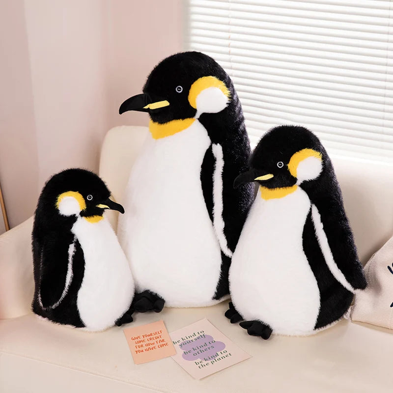 A trio of black and white penguin plush toys sitting on a light-colored sofa.