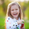 A smiling young girl wearing a white shirt adorned with colorful star embroidery patches.