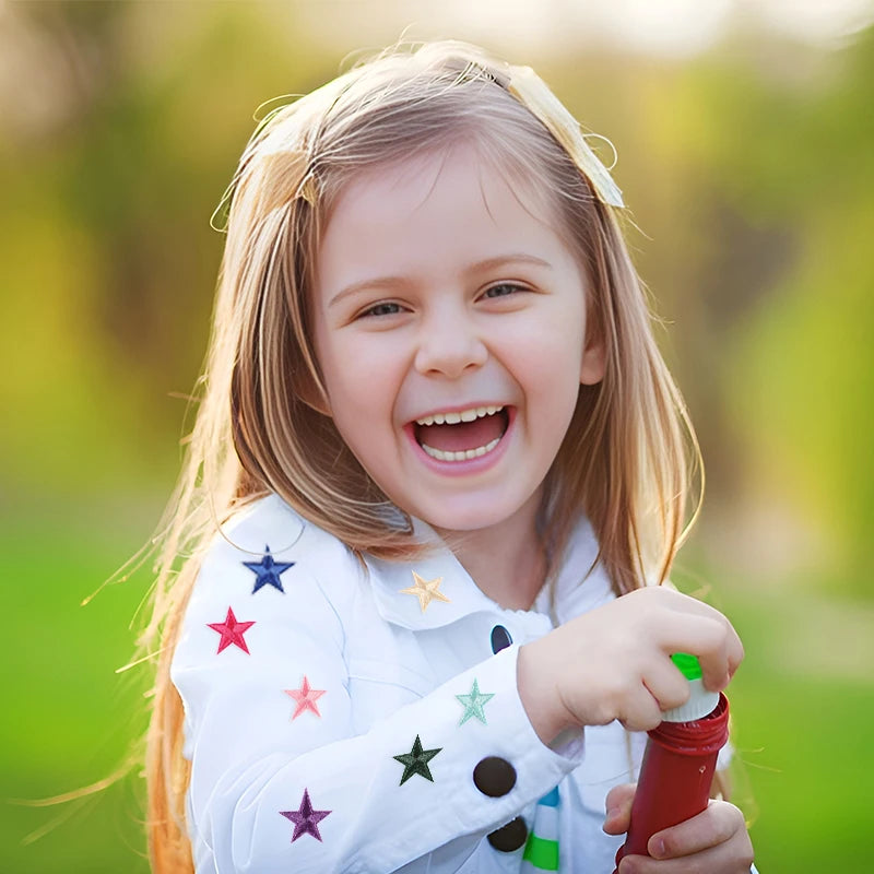 A smiling young girl wearing a white shirt adorned with colorful star embroidery patches.