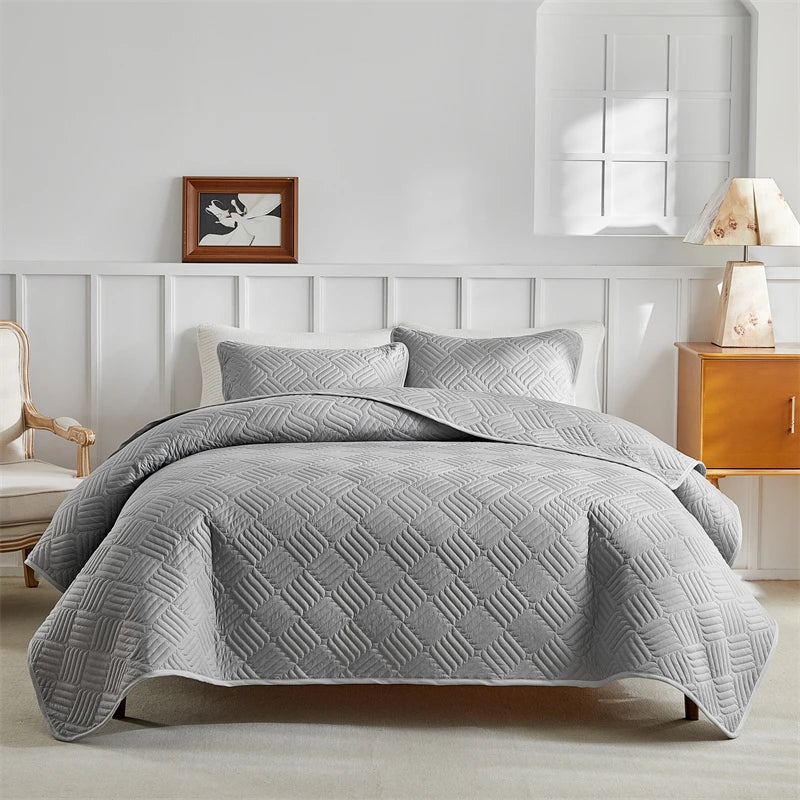 A gray lightweight queen quilt bedding set displayed on a bed with white paneled headboard.