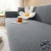 A gray jacquard sofa cover featuring a white, petal-shaped accent cushion with an orange mug on the fabric.