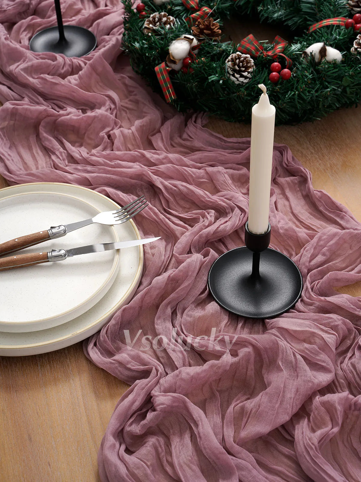 A rustic holiday setting featuring a candle, greenery, and a pink crinkle cheesecloth table runner.