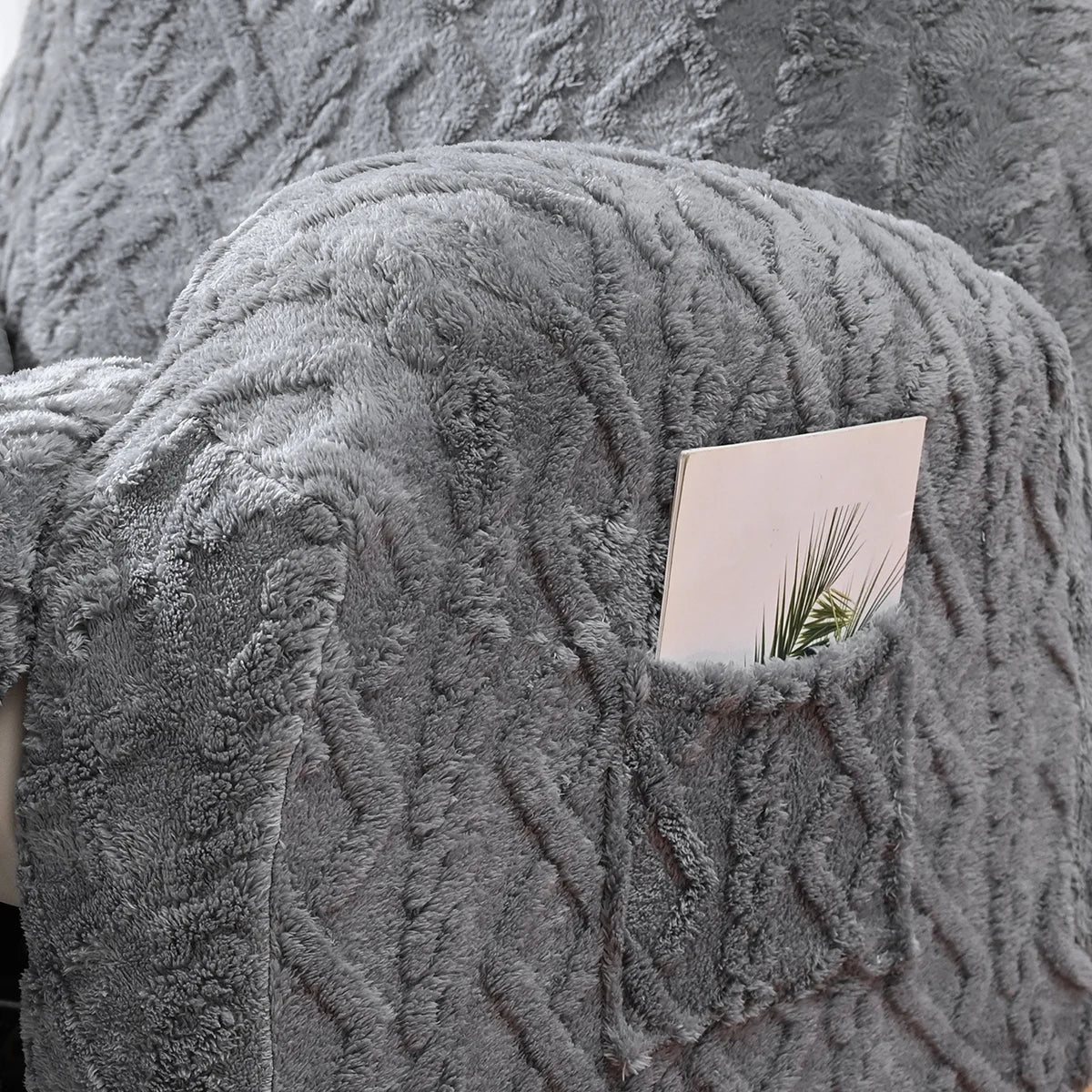 A close-up of a gray faux fur sofa cover featuring a textured, knitted pattern with a small card tucked into the fabric.