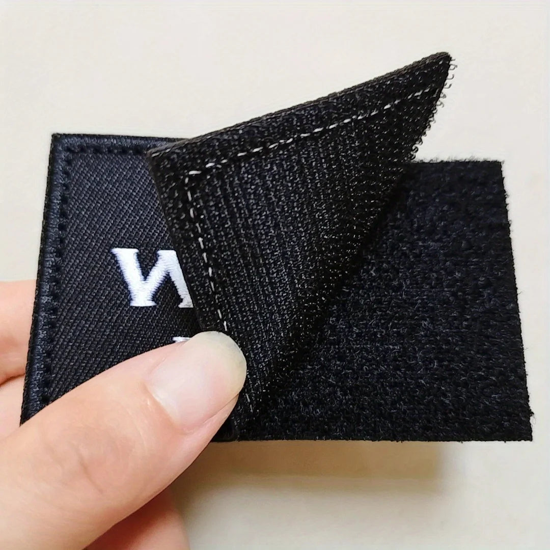 A close-up of a black tactical embroidered patch with a white letter 'N' on a hand.