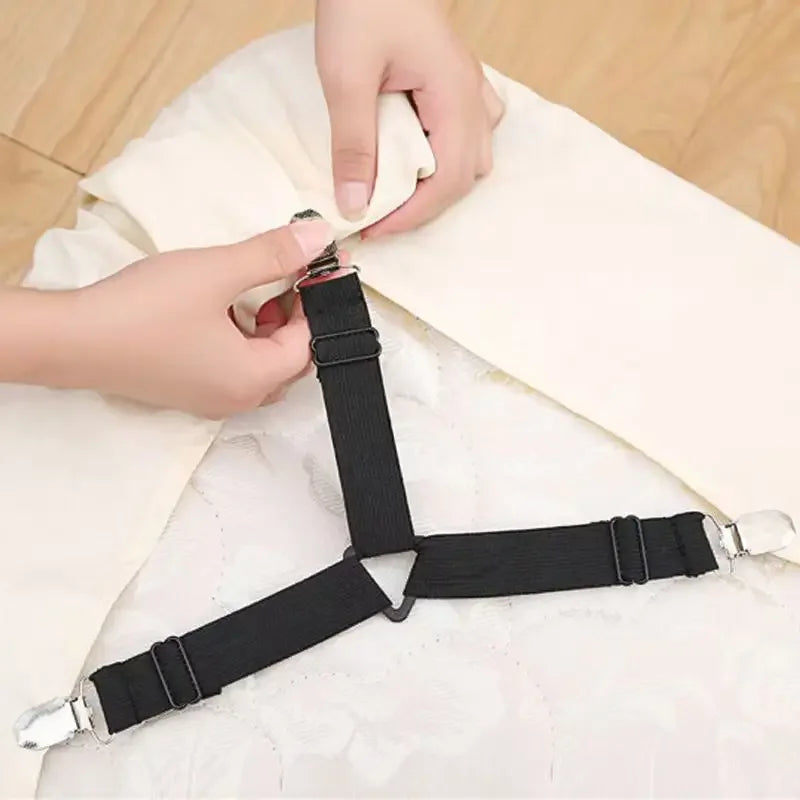 Hands are adjusting black adjustable crisscross bed sheet clips on a white fabric.