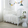 White wooden crib with ruffled skirt and hanging pennants in a bright nursery