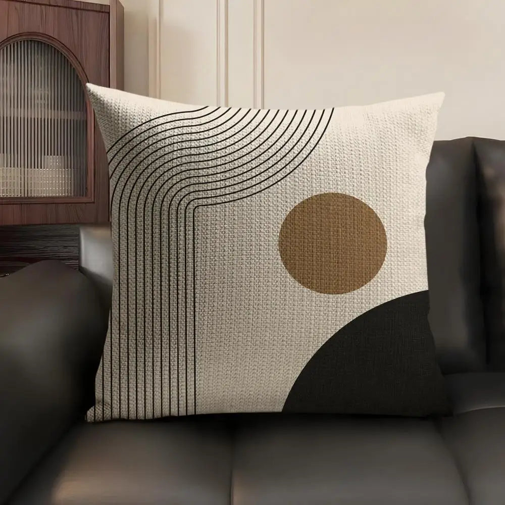 A beige cushion cover featuring black geometric lines and a circular tan accent on a dark sofa.